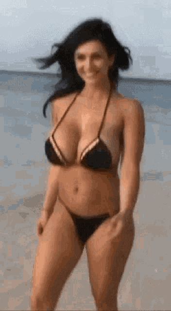 a woman in a bikini is walking on the beach and smiling .