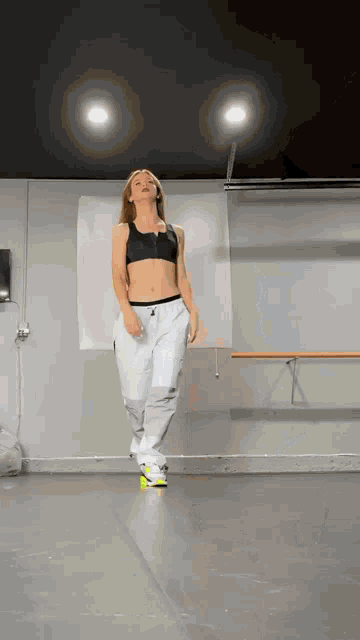 a woman in a black top and white sweatpants is dancing in a dance studio