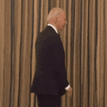 a man in a suit and tie is smiling while standing in front of a curtain .