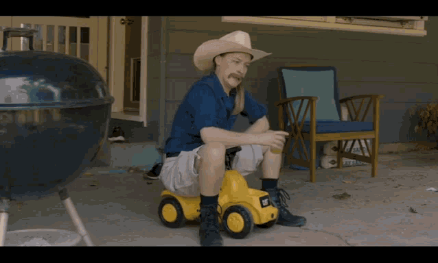 a man wearing a cowboy hat sits on a yellow toy cat truck