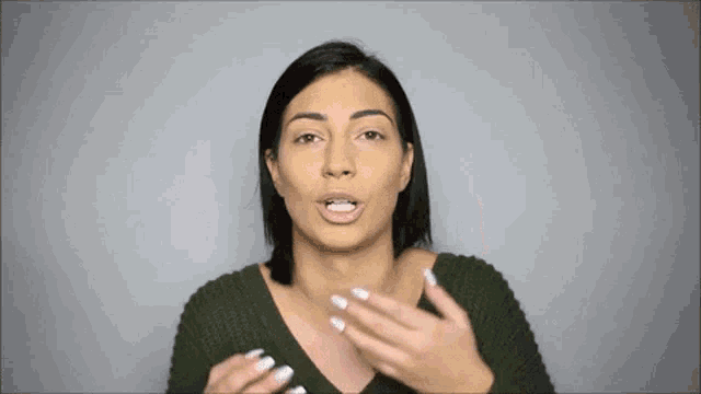 a woman in a green sweater is making a funny face and talking to the camera .