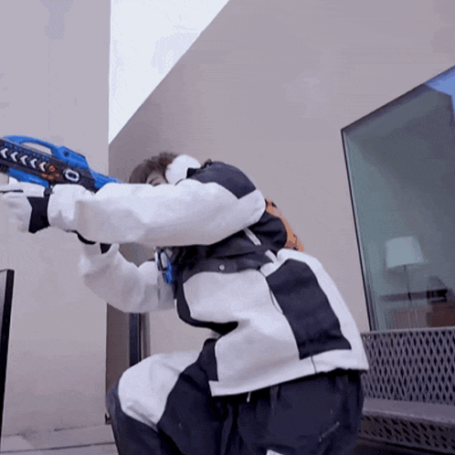 a man in a white and black jacket is holding a blue toy gun with the letter o on it