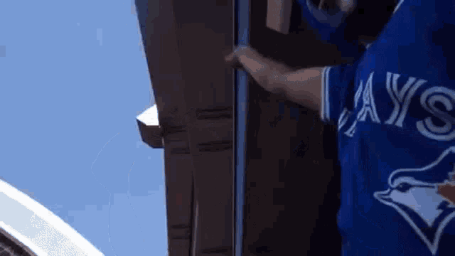a man wearing a blue jays jersey is standing next to a building .