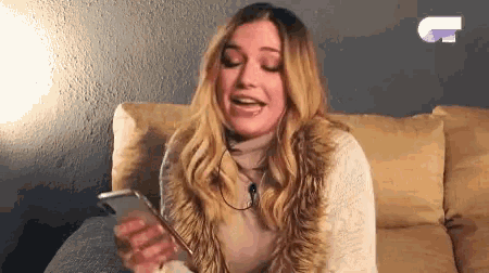 a woman is sitting on a couch looking at her cell phone .