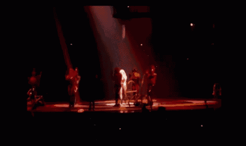 a woman stands on a stage in front of a group of dancers