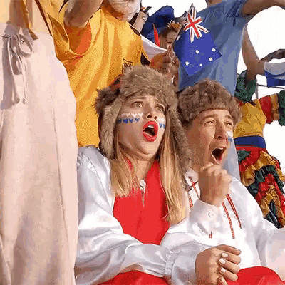 a group of people are sitting in a stadium watching a game and one of them is wearing a fur hat