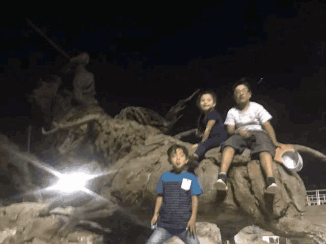 three young boys are sitting on a large rock in the dark