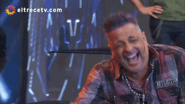 a man in a plaid shirt is laughing in front of a eltrecetv.com logo