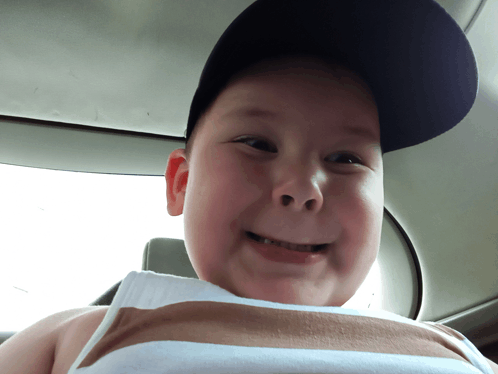 a young boy wearing a baseball cap and a tank top smiles for the camera