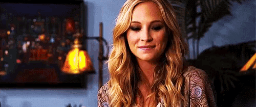 a woman with long blonde hair is smiling in a room with a lamp in the background .