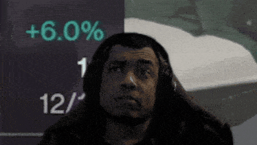 a man wearing headphones is looking up at a screen that says +6.0 %