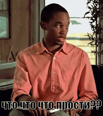 a man in a pink shirt is sitting in front of a window with the words " что что просто ? " on the bottom