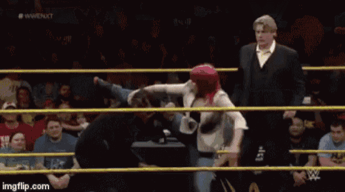 a man in a suit is standing in a wrestling ring with a woman .