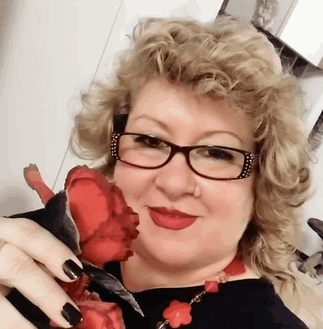 a woman wearing glasses and red lipstick holds a red rose