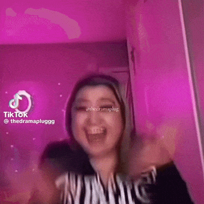 a woman is laughing with her mouth open in front of a pink background .