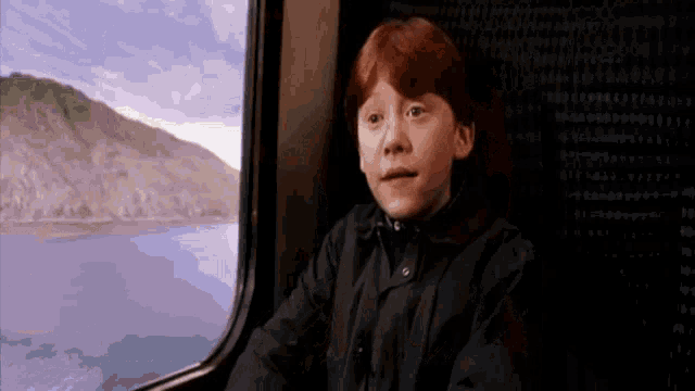 a young boy with red hair is looking out a window on a train