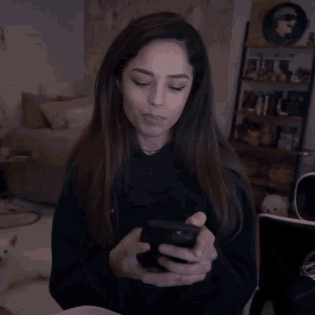 a woman in a green sweatshirt is holding a cell phone