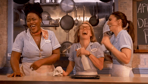 three waitresses are laughing in a kitchen and one has a name tag that says charlie