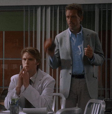 a man in a suit stands next to a man in a lab coat who is covering his mouth with his hands