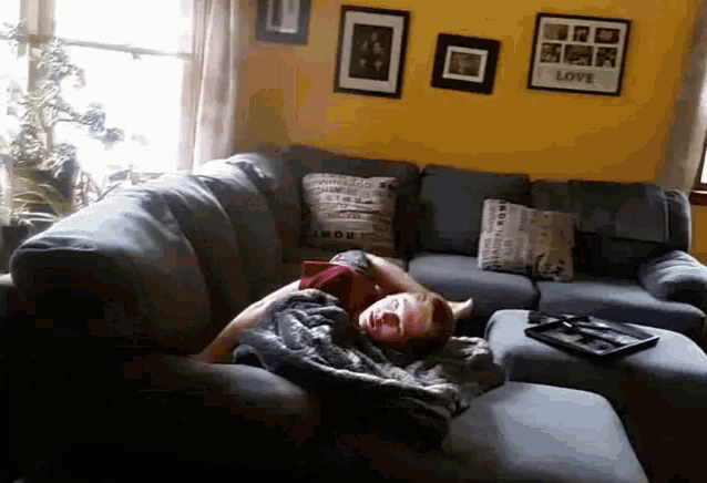 a person laying on a couch in front of a yellow wall with a picture that says love