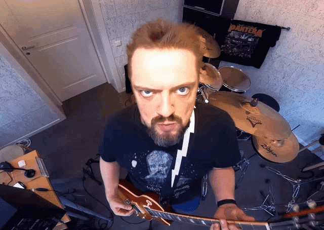 a man playing a guitar in a room with a pantera shirt hanging on the wall