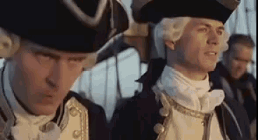 two men in military uniforms and hats are standing next to each other on a ship .