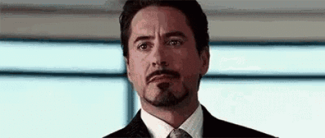 tony stark is wearing a suit and tie and looking at the camera .