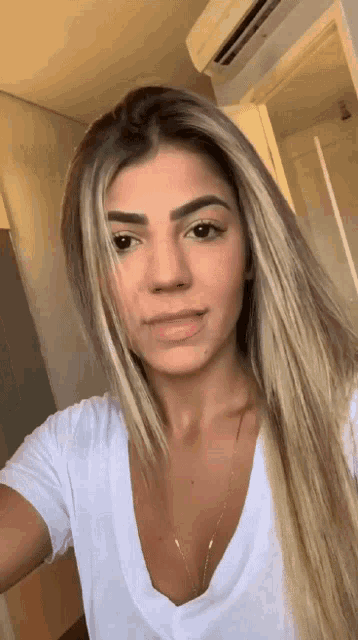 a woman with long blonde hair is wearing a white shirt and taking a selfie