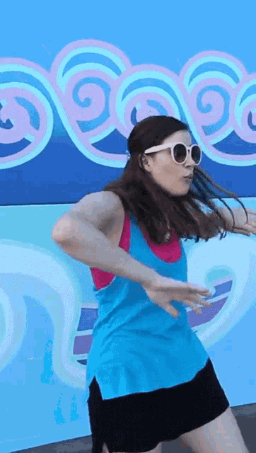 a woman wearing sunglasses is dancing in front of a wall with swirls on it