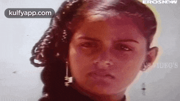 a young girl with curly hair and earrings is looking at the camera .