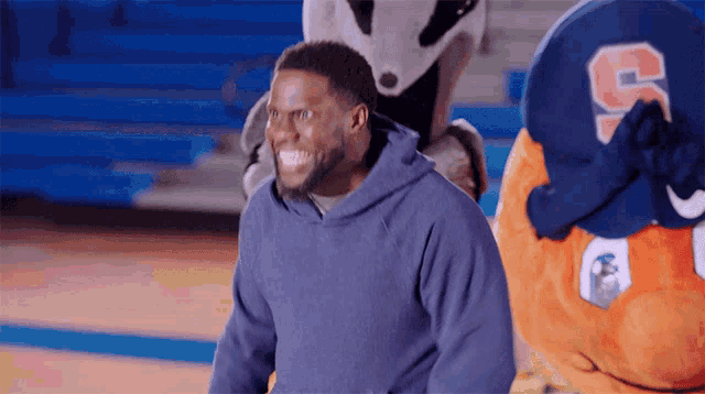 a man in a blue hoodie is standing in front of a mascot with the letter s on it