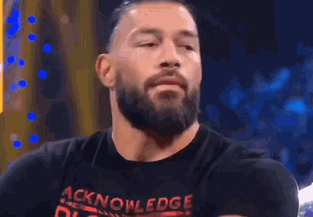 a man with a beard is wearing a black t-shirt that says acknoledge bloodline on it .