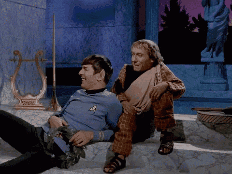 two men are sitting next to each other in a room with a harp and statue in the background