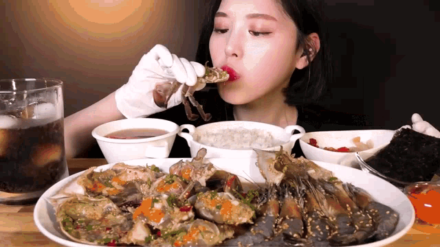 a woman in white gloves is eating crabs and shrimp