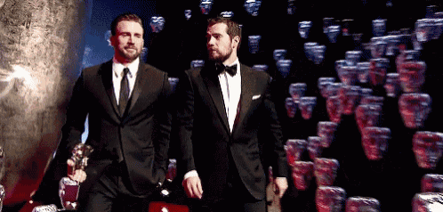 two men in tuxedos and ties are walking down a red carpet .