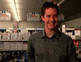 a man in a green shirt is smiling in front of a pharmacy shelf