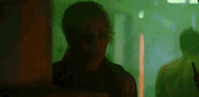 a woman with curly hair is standing in a dark room with green lights .