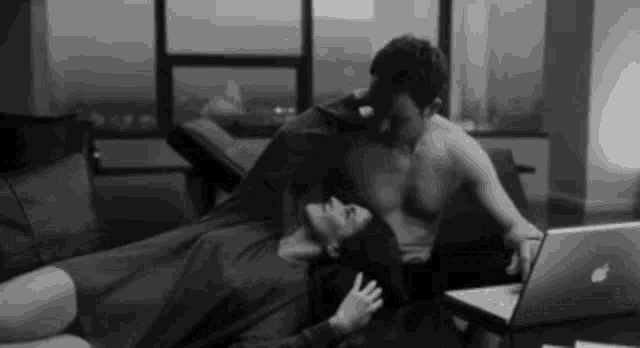 a man and a woman are laying on a couch in front of a laptop .