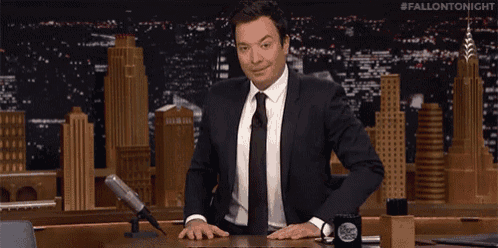a man in a suit and tie is standing in front of a microphone on a fallon tonight show