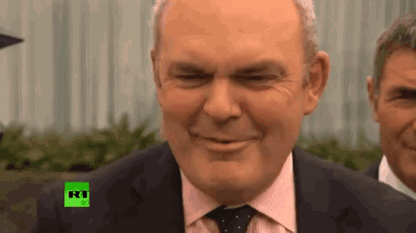 a man in a suit and tie is smiling in front of a rt logo