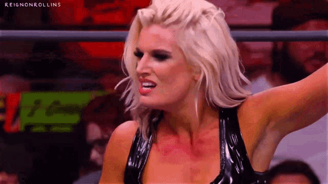 a woman in a black latex dress is standing in a wrestling ring .