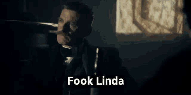 a man in a tuxedo is smoking a cigar in a dark room while holding a bottle of whiskey .