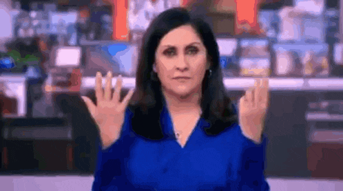 a woman in a blue shirt is making a hand gesture while standing in front of a camera .
