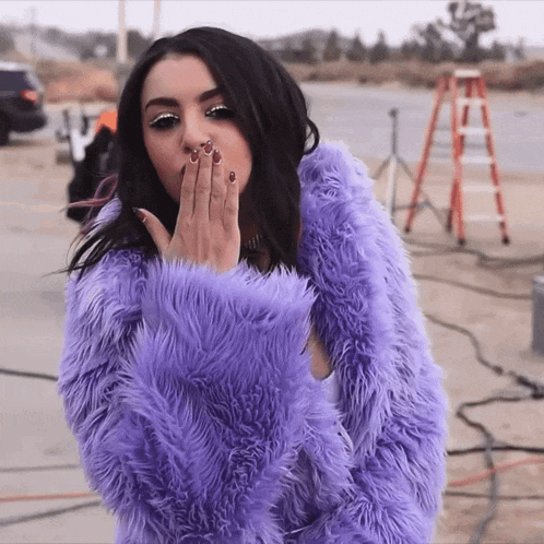 a woman wearing a purple fur coat blowing a kiss