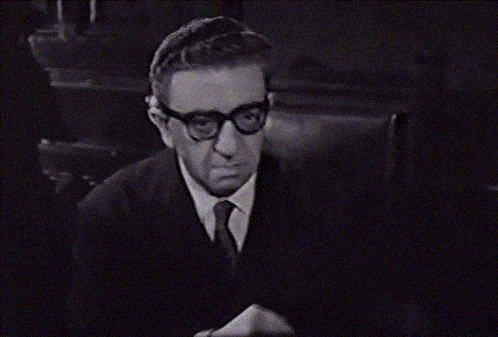 a man in a suit and tie adjusts his glasses in a black and white photo