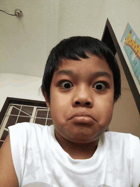 a young boy making a funny face in front of a wall that has a giraffe on it