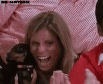 a woman is laughing in a crowd of people while holding a camera .