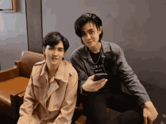 two men are sitting next to each other and one is holding a cell phone