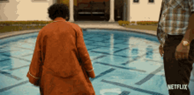 a man in an orange robe walks towards a swimming pool with a netflix logo in the corner