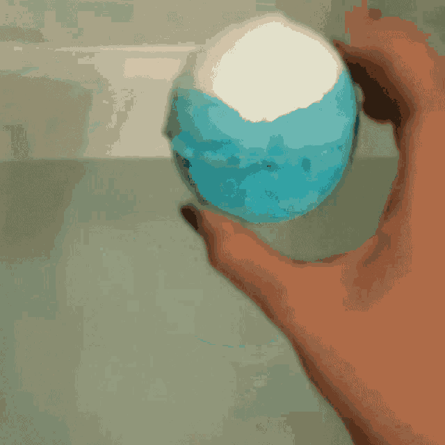 a person is holding a blue bath bomb in their hand in a bathtub